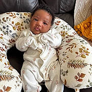 Elora joined the competition — help win amazing prizes! baby, infant, onesie, cushion, leaf_pattern, brown_leather, face, expression, cute, cozy, indoor, furniture, child, person, newborn, soft, seated, home, comfort, portrait