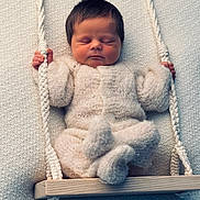 Jaxson is registered to the contest to win money with this photo: newborn, baby, sleeping, knitted_outfit, swing, rope, wooden_swing, cozy, soft_texture, peaceful, infant, child, cute, hands, feet, portrait, indoors, warm, resting, adorable