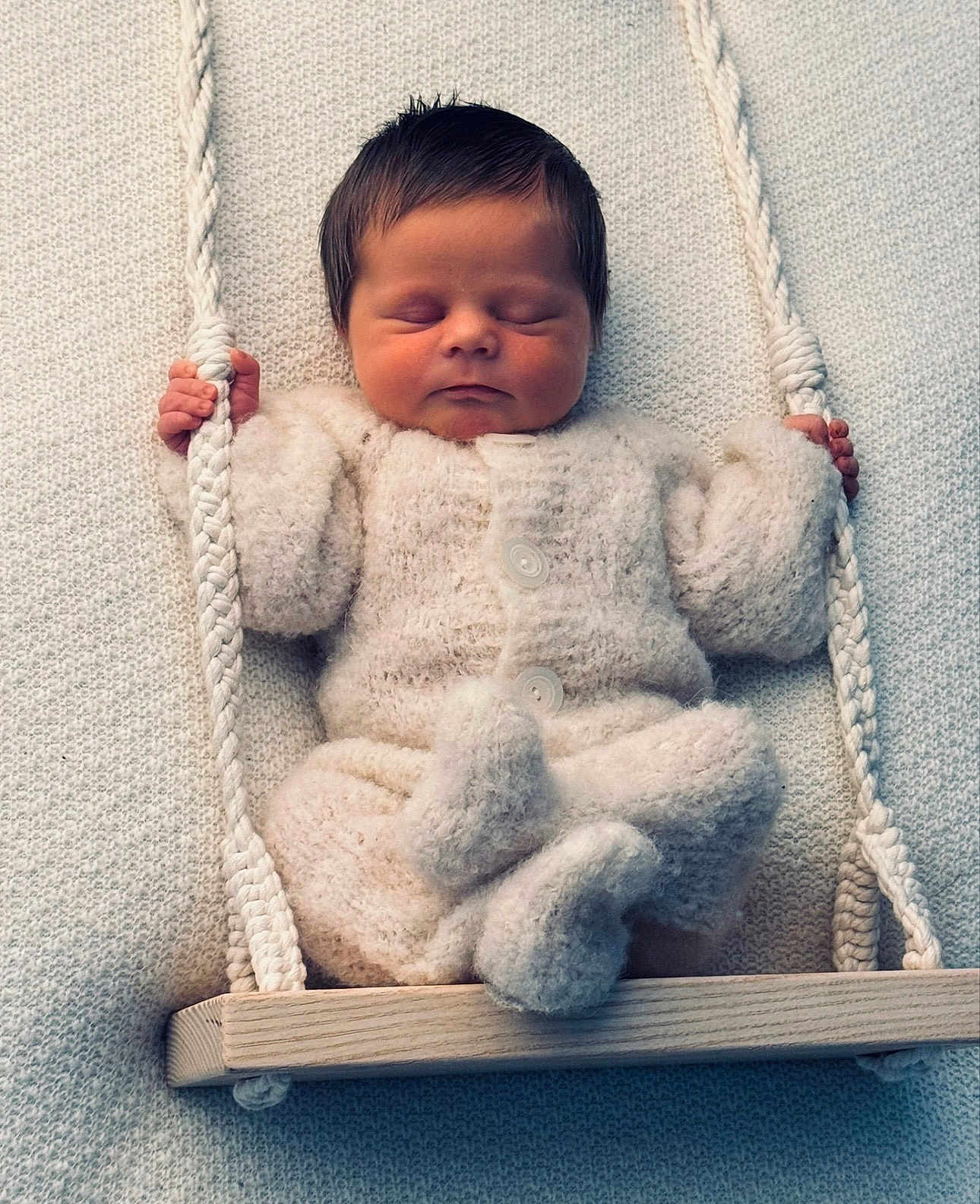 Jaxson is registered to the contest to win money with this photo: newborn, baby, sleeping, knitted_outfit, swing, rope, wooden_swing, cozy, soft_texture, peaceful, infant, child, cute, hands, feet, portrait, indoors, warm, resting, adorable