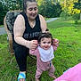 baby, bib, chair, child, footwear, grass, greenery, happy, holding_hands, nature, onesie, outdoor, parenting, person, road, smile, sunlight, tattoo, tree, woman