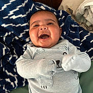Kyeson is registered to the contest to win money with this photo: baby, infant, smiling, laughing, pajamas, blanket, blue, white, face, hands, bed, bedding, cozy, cute, child, person, indoors, wood, pattern, happy
