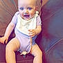 baby, child, smiling, sitting, couch, onesie, bib, indoor, happy, cute, infant, furniture, skin, foot, hand, head, blue_eyes, giraffe, pacifier, relaxed