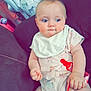 baby, infant, blue_eyes, onesie, bib, pacifier, red_clip, couch, indoor, child, cute, plump, seated, looking_away, soft_lighting, baby_carrier, fabric_pattern, hand, foot, skin