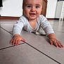 baby, crawling, floor, indoor, happy, smiling, child, person, white_clothing, tile, hands, head, eyes, mouth, wooden_door, cabinet, home, cute, infant, portrait