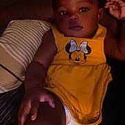 Sky is registered to the contest to win money with this photo: child, baby, yellow_dress, minnie_mouse, pillow, indoor, relaxed, portrait, infant, hand, face, dark_background, couch, diaper, person, cute, clothing, young, comfortable, soft_lighting