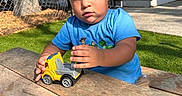 Gael joined the competition — help win amazing prizes! backyard, blue_shirt, casual_clothing, chain_link_fence, child, curly_hair, daylight, expression, grass, nature, outdoor, person, picnic_table, playing, sunlight, toddler, toy, toy_truck, wooden_table, young_child