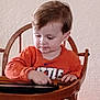 Myles is registered to the contest to win money with this photo: casual_clothing, child, childhood, concentration, furniture, hands, high_chair, home, indoor, light_brown_hair, looking_down, orange_shirt, person, playing, seated, tablet, toddler, wall, wooden_chair, young_child