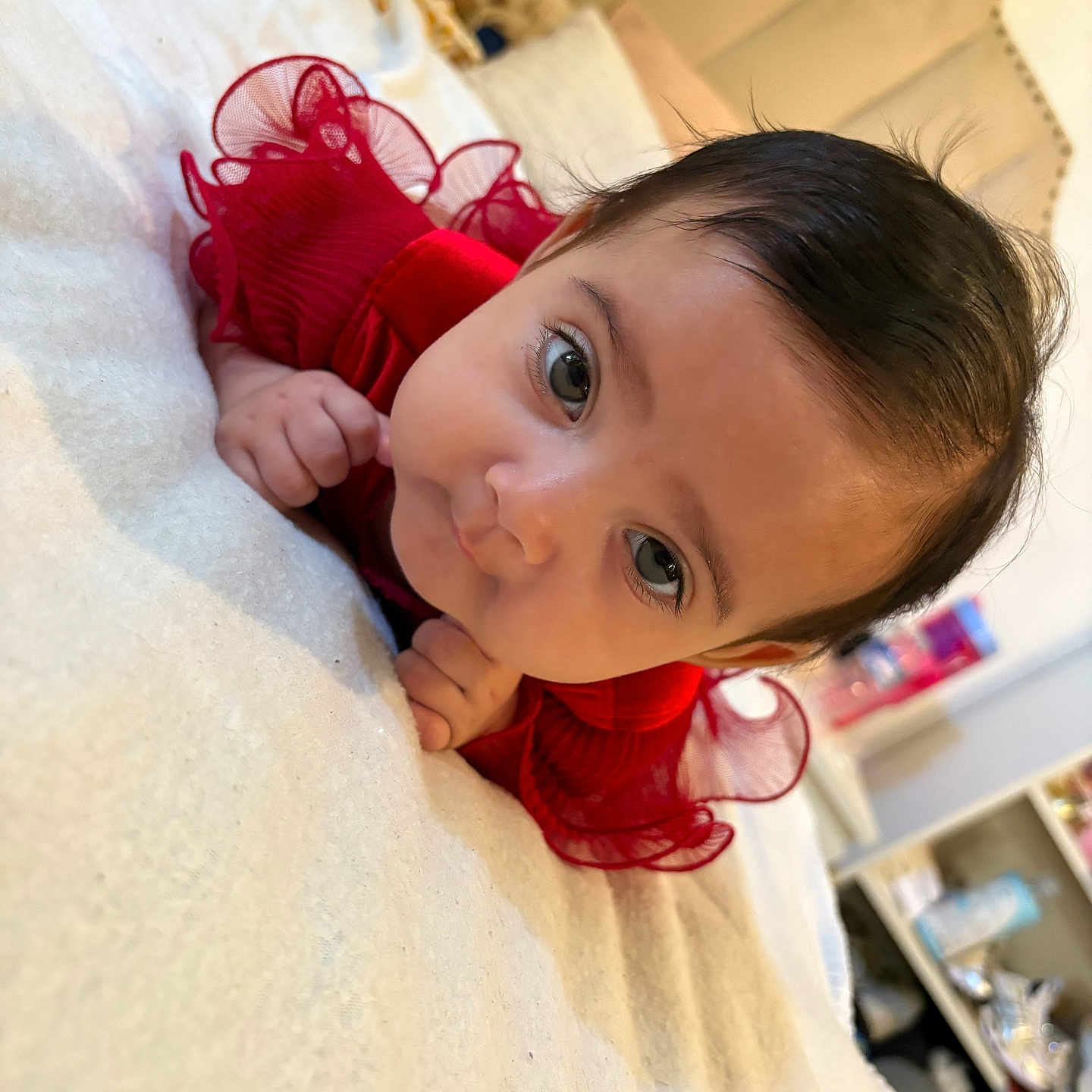 Hasna a rejoint le concours — aidez-le/la à gagner de superbes lots ! baby, baby_girl, bed, bedroom, blanket, child, clothing, curious, cute, eyes, face, hands, home, indoors, infant, lying_down, person, portrait, red_dress, soft