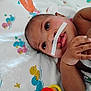 baby, infant, face, hands, medical_tape, blanket, duck_pattern, toy, colorful, lying_down, close_up, skin, child, cute, eyes, expression, indoors, soft_toy, newborn, healthcare