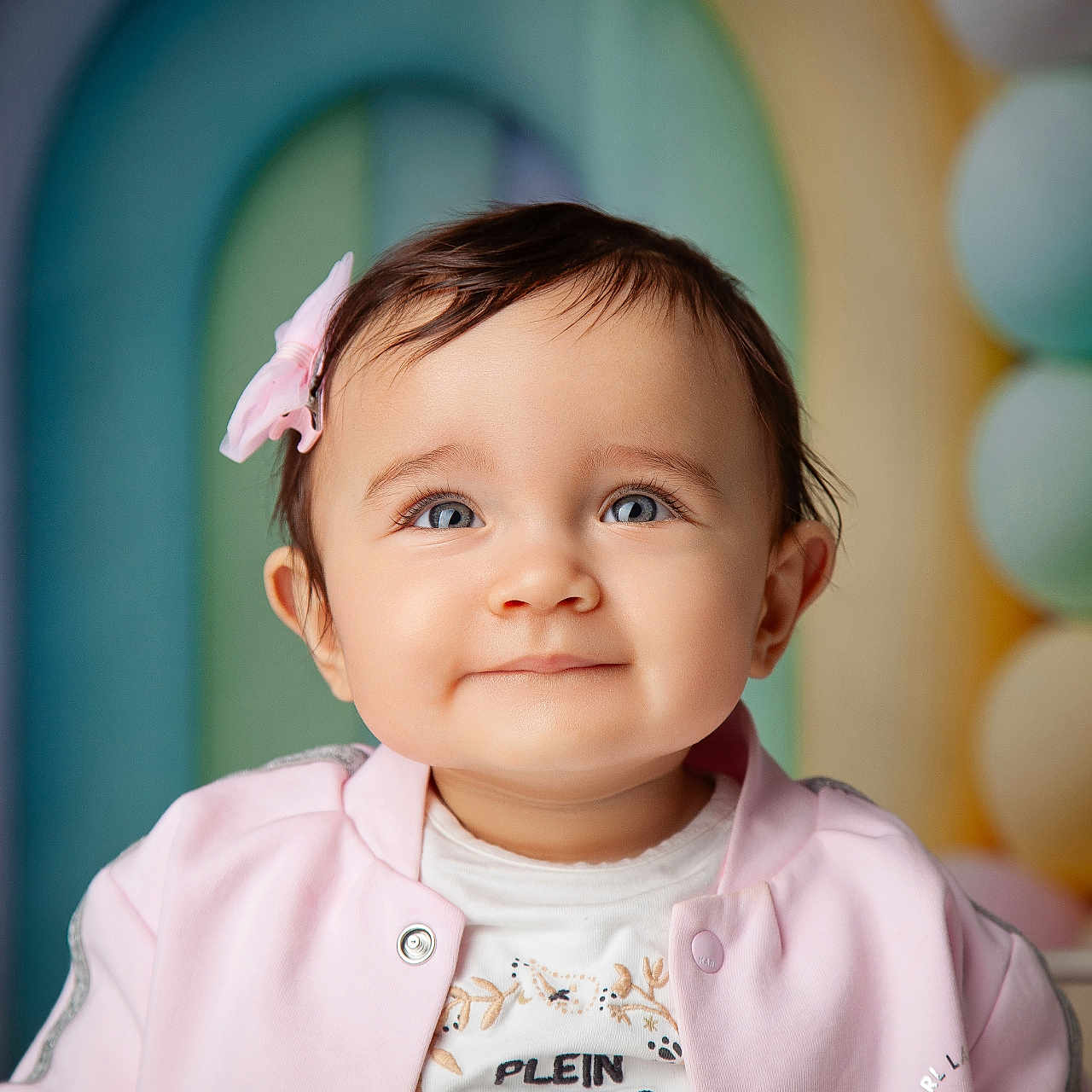 Emma a rejoint le concours — aidez-le/la à gagner de superbes lots ! baby, background, balloons, blue_eyes, child, colorful, cute, face, happy, headshot, indoors, infant, jacket, person, pink_bow, portrait, smiling, soft_lighting, white_shirt, young_child
