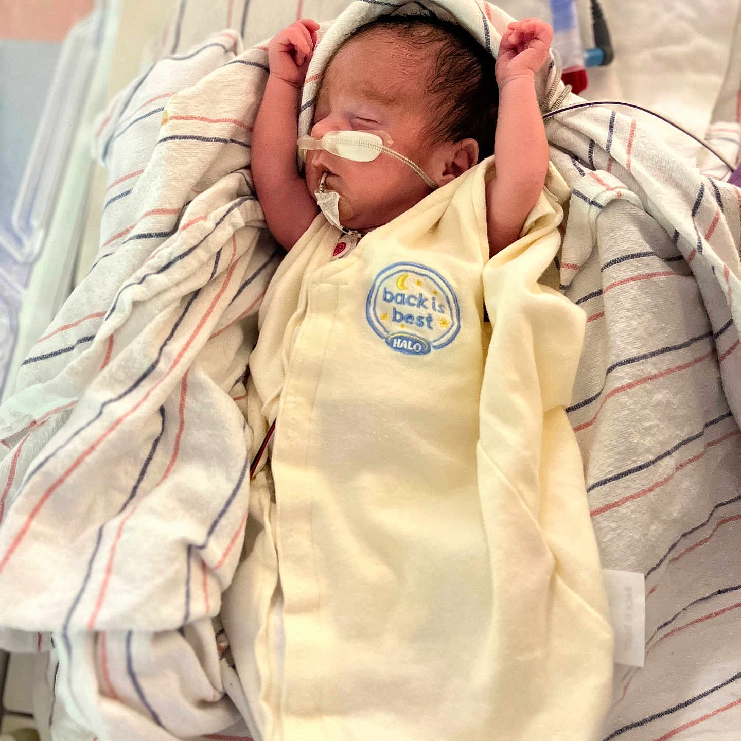 Maximillion is registered to the contest to win money with this photo: newborn, baby, infant, sleeping, blanket, hospital, crib, medical_tubes, yellow_onesie, striped_blanket, peaceful, wrapped, arms_up, soft_fabric, cute, healthcare, portrait, indoors, person, child