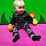 Rae is registered to the contest to win money with this photo: toddler, child, baby, sitting, playground, colorful, ball, overalls, pink_mat, green_background, flower, leaves, black_socks, smiling, indoor, cute, young_child, playing, happy, casual_clothing