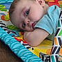 Liam is registered to the contest to win money with this photo: baby, child, play_mat, blue_shirt, floor, indoor, infant, resting, face, head, skin, person, cute, young, colorful, pattern, soft, closeup, portrait, sleepy