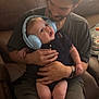 Liam joined the competition — help win amazing prizes! baby, man, headphones, blue_headphones, indoor, couch, brown_couch, person, infant, holding, seated, casual_clothing, shorts, tshirt, watch, curious_expression, child, family, love, comfortable