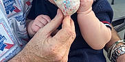 Liam joined the competition — help win amazing prizes! baby, child, toddler, person, hand, face, food, treat, sprinkles, clothing, socks, adult, watch, bracelet, sitting, outdoor, background, blurred_person, festival, feeding