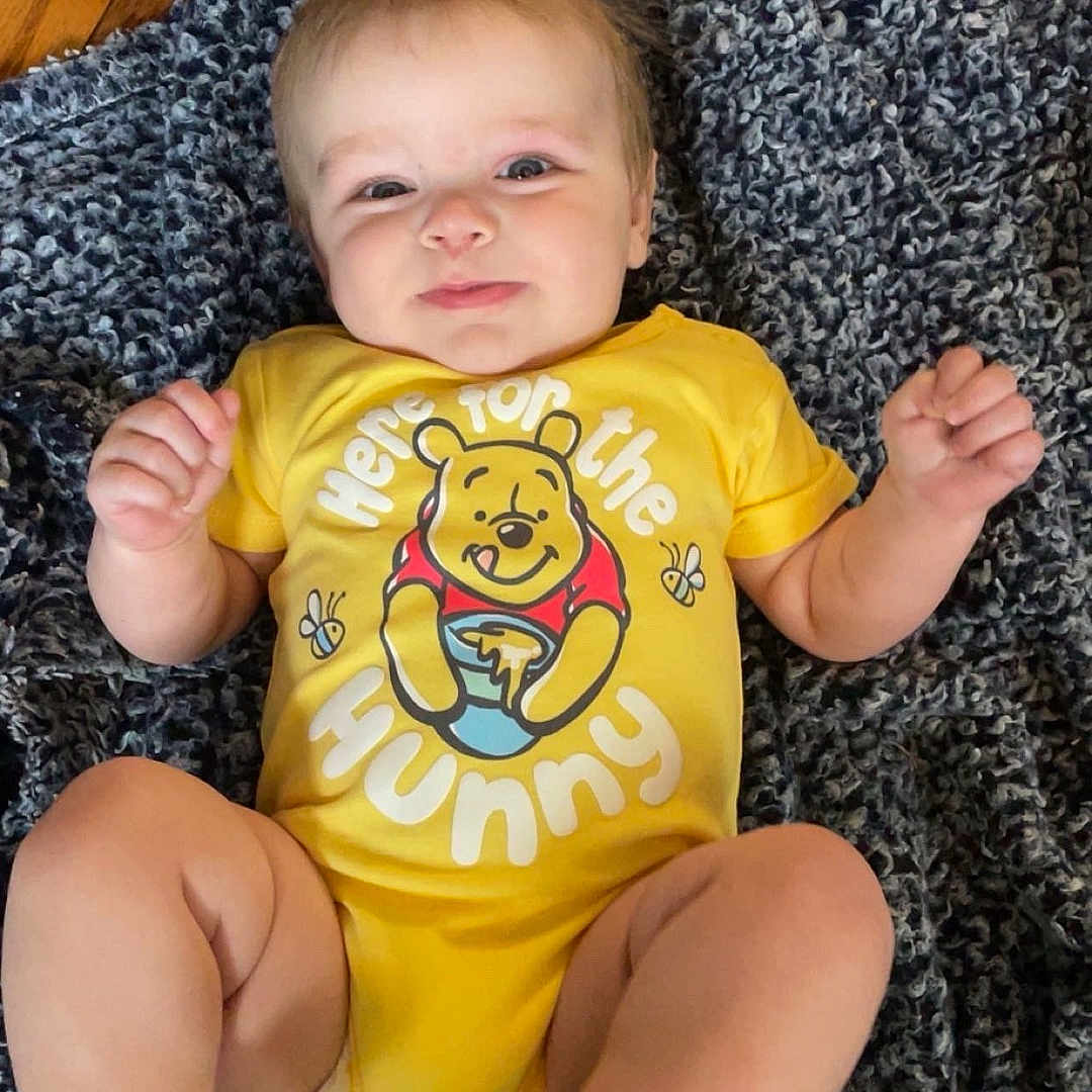 Liam is registered to the contest to win money with this photo: baby, blanket, child, clothing, cute, fist, floor, foot, happy, indoors, infant, lying_down, person, portrait, skin, smile, toddler, winnie_the_pooh, wooden_floor, yellow_onesie