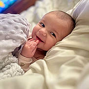 Aurora is registered to the contest to win money with this photo: baby, smiling, blanket, bed, pillow, infant, cute, face, hand, soft, cozy, child, lying_down, indoors, happy, young, portrait, skin, expression, comfort