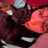 Cheeto is registered to the contest to win money with this photo: black_cat, cat, pet, human, face, lying_down, cuddling, close_up, indoor, affection, cozy, resting, portrait, animal, person, bed, blanket, soft_lighting, warm_colors, piercing