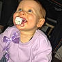 baby, child, pacifier, lavender_sweater, bow, smile, blue_eyes, rosy_cheeks, toddler, indoor, flash_photography, candid, cute, portrait, sitting, clothing, young_child, happy, family_moment, closeup
