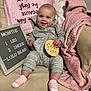 baby, infant, smiling, gray_outfit, pink_blanket, wooden_sign, chair, cozy, cute, happy, indoor, person, child, face, sock, plush_blanket, text_board, baby_milestone, couch, portrait
