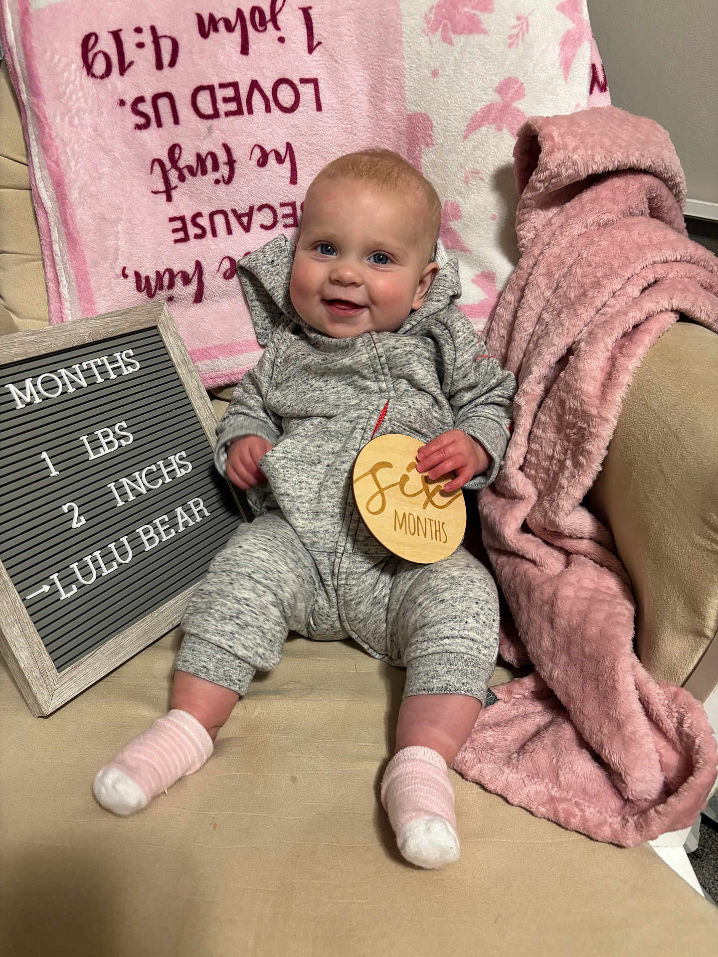 Luella joined the competition — help win amazing prizes! baby, infant, smiling, gray_outfit, pink_blanket, wooden_sign, chair, cozy, cute, happy, indoor, person, child, face, sock, plush_blanket, text_board, baby_milestone, couch, portrait