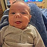 Jett is registered to the contest to win money with this photo: baby, child, infant, portrait, face, smiling, tongue_out, indoors, home, knitwear, cardigan, clothing, seated, close_up, television, shelves, denim, cozy, family_photo, happy