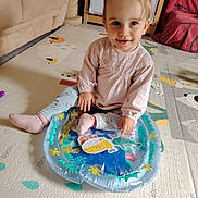 Amalya a rejoint le concours — aidez-le/la à gagner de superbes lots ! toddler, child, indoor, playmat, inflatable_toy, pink_socks, long_sleeve_shirt, patterned_pants, pigtails, smiling, floor_mat, living_room, sofa, playtime, cute, young_child, home, floor, toy, happy