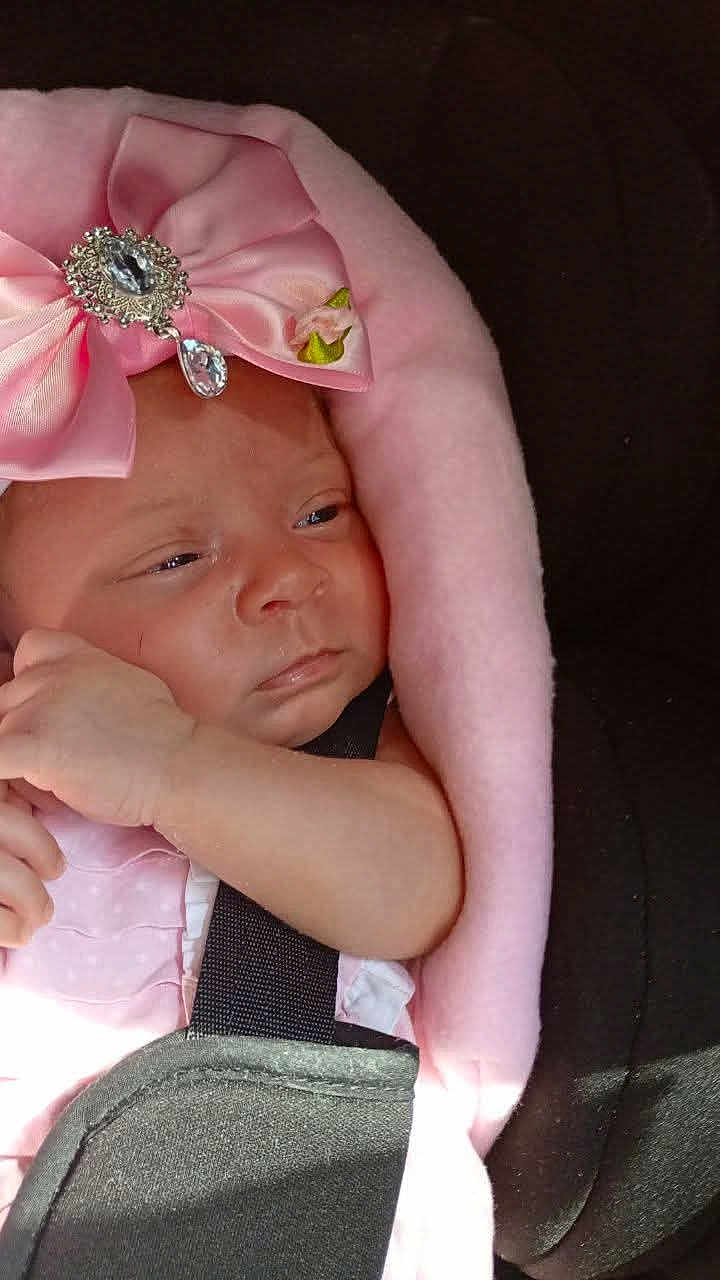 Jeanie-Marie is registered to the contest to win money with this photo: baby, infant, pink_bow, blanket, car_seat, child, face, headwear, straps, soft_texture, adorable, small_hand, clothing, portrait, newborn, cute, resting, indoors, closeup, skin