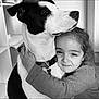 child, dog, hugging, black_and_white, indoor, affection, pet, smiling, close_up, collar, fur, sleeve, shelf, papers, calm, face, happy, young, gentle, friendship