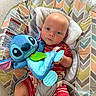 Cody is registered to the contest to win money with this photo: baby, child, plush_toy, stitch_toy, blue_toy, red_clothing, striped_outfit, baby_seat, patterned_fabric, soft_texture, indoor, carpet, comfort, cute, infant, holding_toy, portrait, person, young_child, colorful