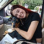 woman, dog, car_interior, smiling, affection, pet, red_hair, black_dog, tan_markings, casual_clothing, gold_chain, piercing, window, outdoor_background, seat, human_animal_bond, happy, portrait, candid, love