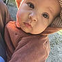 baby, child, face, hood, brown_clothing, outdoor, sunlight, curious_expression, closeup, person, cute, infant, young_child, fuzzy_outfit, portrait, warm_clothing, car, grass, daylight, nature
