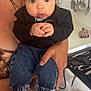 baby, child, person, indoor, kitchen, holding, jeans, black_sweater, hair_tie, wide_eyes, expression, adult_hand, utensils, washing_machine, appliance, countertop, clothing, barefoot, curly_hair, skin