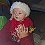baby, child, santa_hat, red_clothing, adult_hand, indoor, holiday, festive, toy, carpet, sweater, cozy, smiling, cute, infant, person, holding, winter_wear, holiday_season, home
