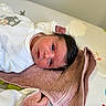 newborn, baby, infant, towel, white_clothing, animal_embroidery, face, dark_hair, lying_down, changing_pad, curious_eyes, soft_texture, indoors, cute, resting, skin, hand, blanket, baby_clothes, peaceful