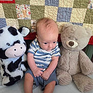Hunter joined the competition — help win amazing prizes! baby, infant, striped_shirt, plush_toy, cow_plush, teddy_bear, quilt, patchwork, bed, cute, child, soft_toy, sitting, indoors, fabric, colorful, toy, person, young_child, cozy