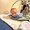 baby, infant, striped_onesie, blanket, smiley_faces, baby_gym, plush_elephant, toy, floor, indoor, child, tummy_time, play, happy, cute, person, soft_toys, furniture, home, warm_lighting