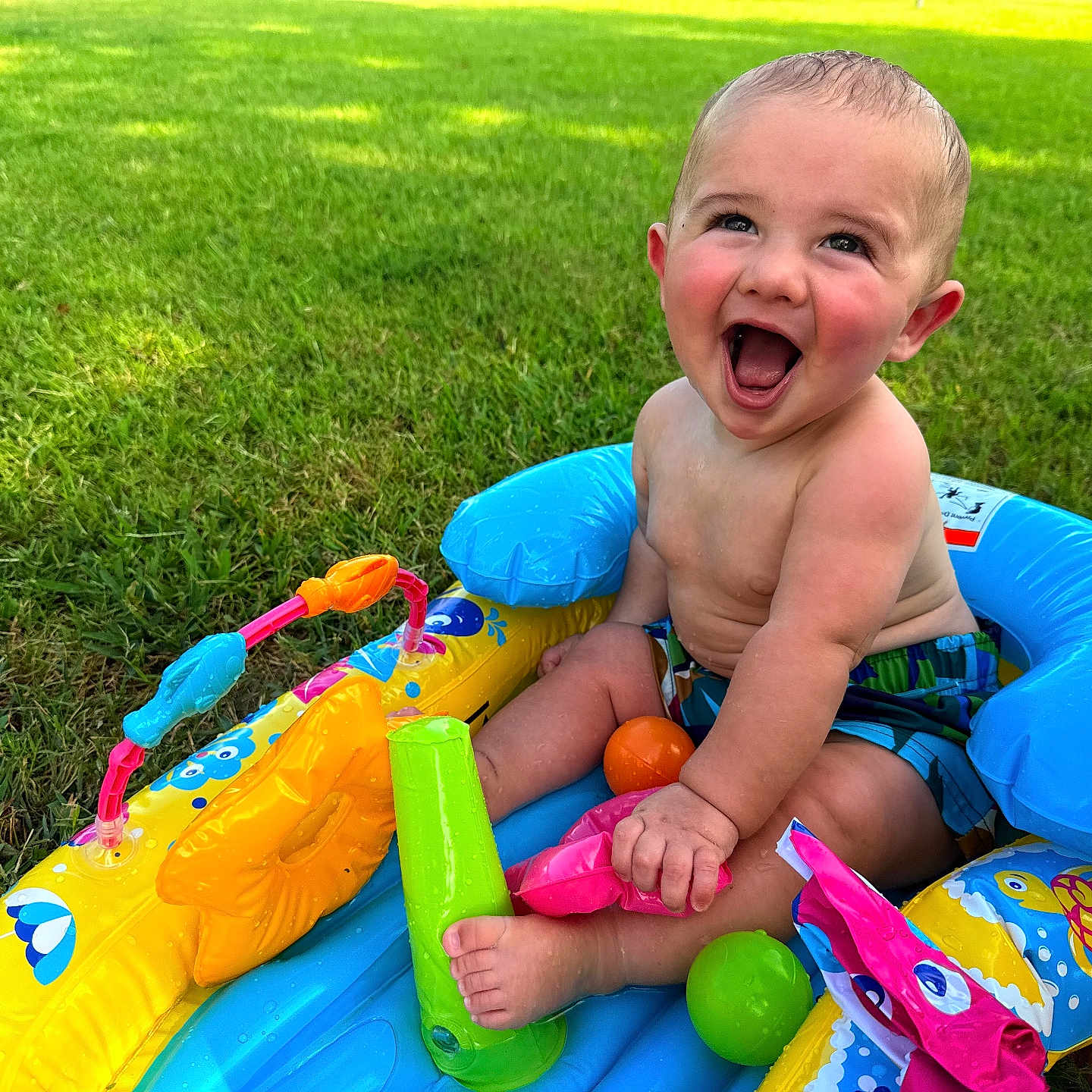 Aryn is registered to the contest to win money with this photo: baby, child, inflatable_pool, grass, outdoor, summer, toy, colorful, happy, laughing, bare_chest, playtime, greenery, sunlight, water_toy, sitting, cute, fun, infant, nature