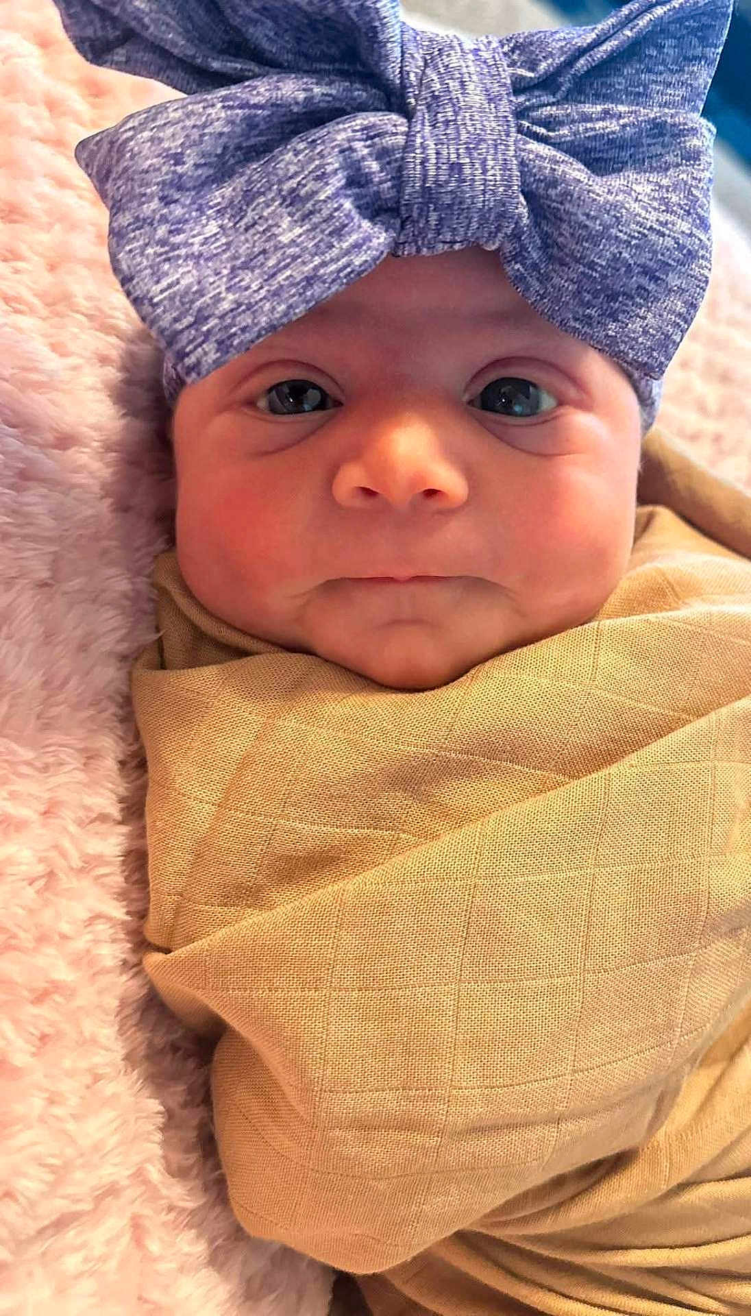 Amara joined the competition — help win amazing prizes! baby, infant, face, headband, bow, blanket, wrapped, close_up, pink, beige, soft, texture, newborn, portrait, cute, child, expression, indoors, person, cozy