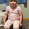 child, pajamas, unicorn, blonde_hair, sitting, chair, carpet, indoor, curtain, smiling, person, young_child, bedroom, casual, home, cute, pale_skin, short_sleeves, pants, relaxed