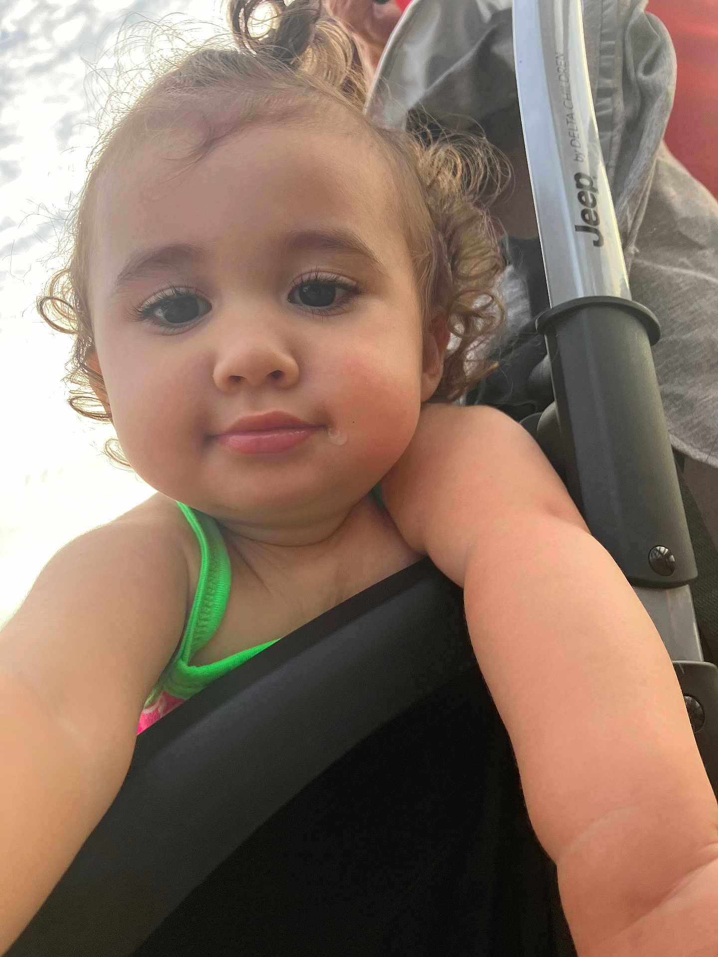 Zamira is registered to the contest to win money with this photo: toddler, child, curly_hair, close_up, selfie, face, arm, stroller, outdoor, sunlight, water_reflection, green_clothing, baby, cute, portrait, person, happy, young_child, skin, daylight