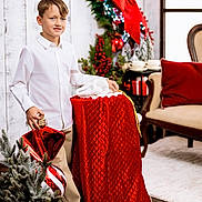 Nathan joined the competition — help win amazing prizes! child, boy, white_shirt, beige_pants, christmas_ornament, holiday_decor, red_bow, greenery, lights, quilted_sack, indoor, wood_floor, chair, smile, festive, celebration, winter, gift, white_shoes, happy