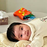 Vivian joined the competition — help win amazing prizes! baby, background_blur, black_hair, blanket, child, curious, cute, face, hand, indoor, infant, knitted, lying_down, portrait, smile, soft_light, table, tissue_box, white_clothing, young