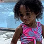 child, curly_hair, smiling, poolside, water, tank_top, pink_clothing, summer, outdoor, playful, person, toddler, young_child, cute, fashion, casual_wear, skin, portrait, daylight, fun