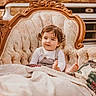 toddler, child, sofa, vintage_furniture, quilt, blanket, curly_hair, indoors, portrait, relaxed, face, clothing, cute, seated, furniture, patterned, old_vehicle, background, warm_tones, casual