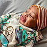 baby, beanie, cartoon_print, child, clothing, cozy, cute, expression, face, happy, hoodie, indoor, infant, laying_down, person, portrait, smiling, soft_light, striped_hat, tongue_out