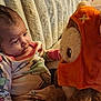 baby, plush_toy, pajamas, curious, stuffed_animal, orange_hood, indoor, blanket, child, cute, soft_toy, seated, cozy, infant, face, expression, warm_lighting, home, comfort, toy