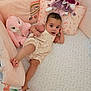 baby, infant, crib, plush_toy, bunny, pillow, blanket, foot, hand, clothing, cute, child, indoor, bedroom, soft_toys, patterned_sheet, relaxing, looking_at_camera, pink, young_child