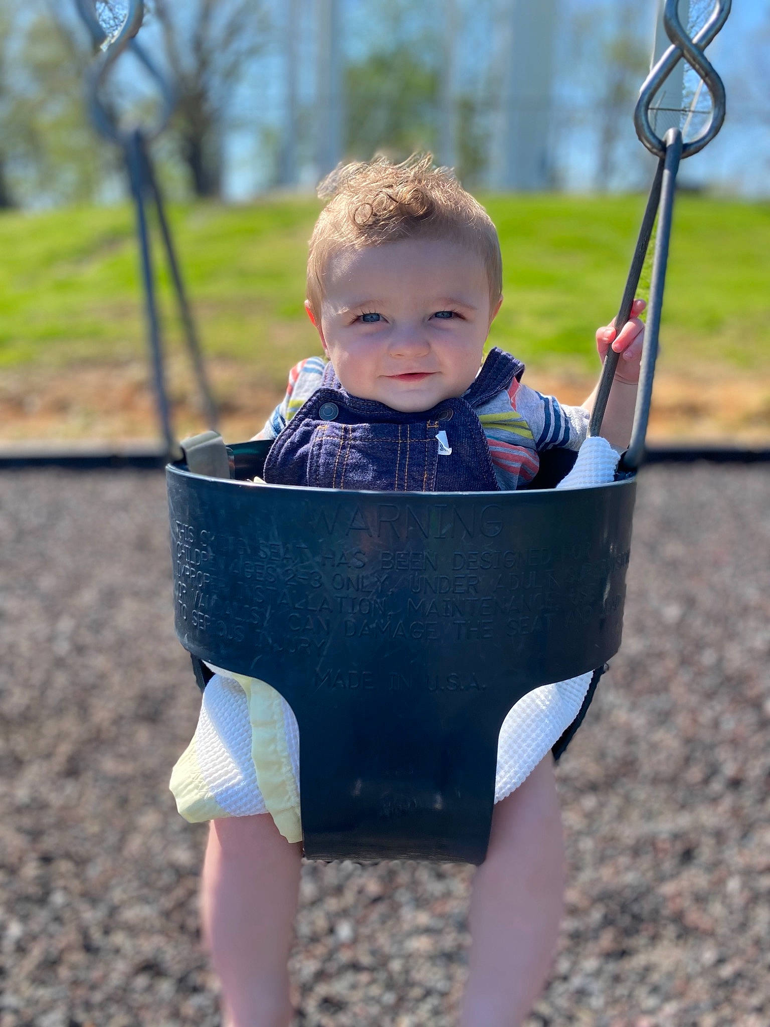 Maxton is registered to the contest to win money with this photo: baby, baby_toddler_clothing, city, electric_blue, face, fun, grass, hand, happy, head, human_body, leisure, people_in_nature, person, plant, playground, recreation, smile, swing, toddler