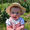 baby, child, smiling, hat, outdoor, flower, tulip, grass, sunlight, nature, greenery, cute, happy, portrait, sitting, pink_overalls, white_shirt, garden, daylight, closeup